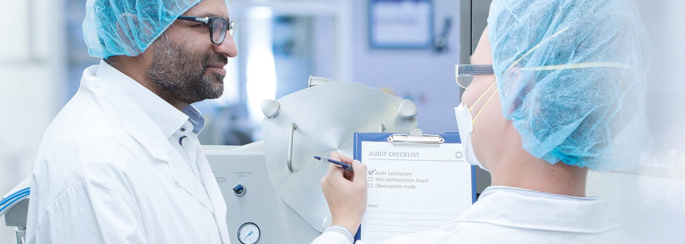 Dwóch pracowników laboratorium w odzieży ochronnej sprawdza razem listę kontrolną w sterylnym środowisku produkcyjnym.