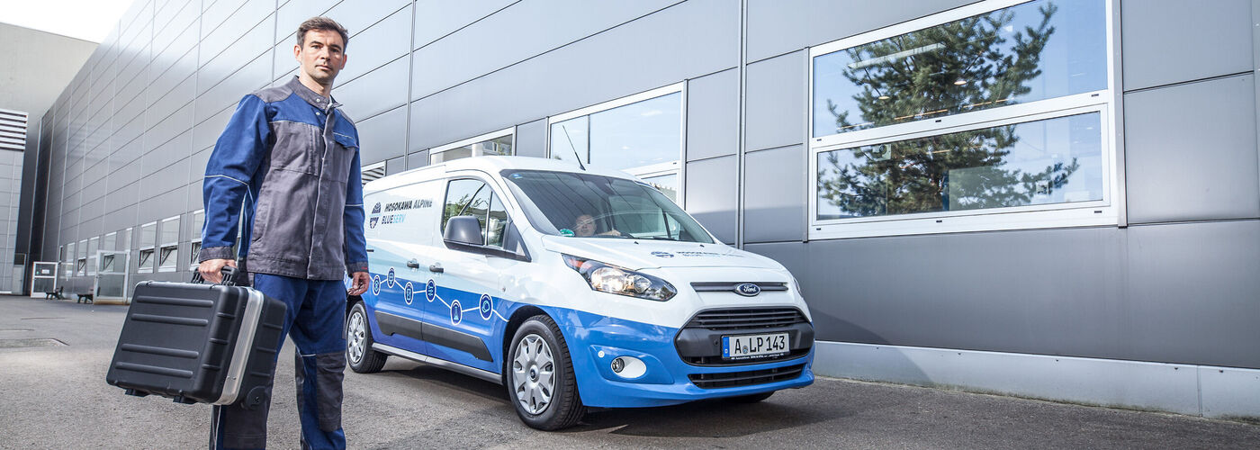 Pracownik serwisu Blueserv ze skrzynką narzędziową stojący przed samochodem Blueserv
