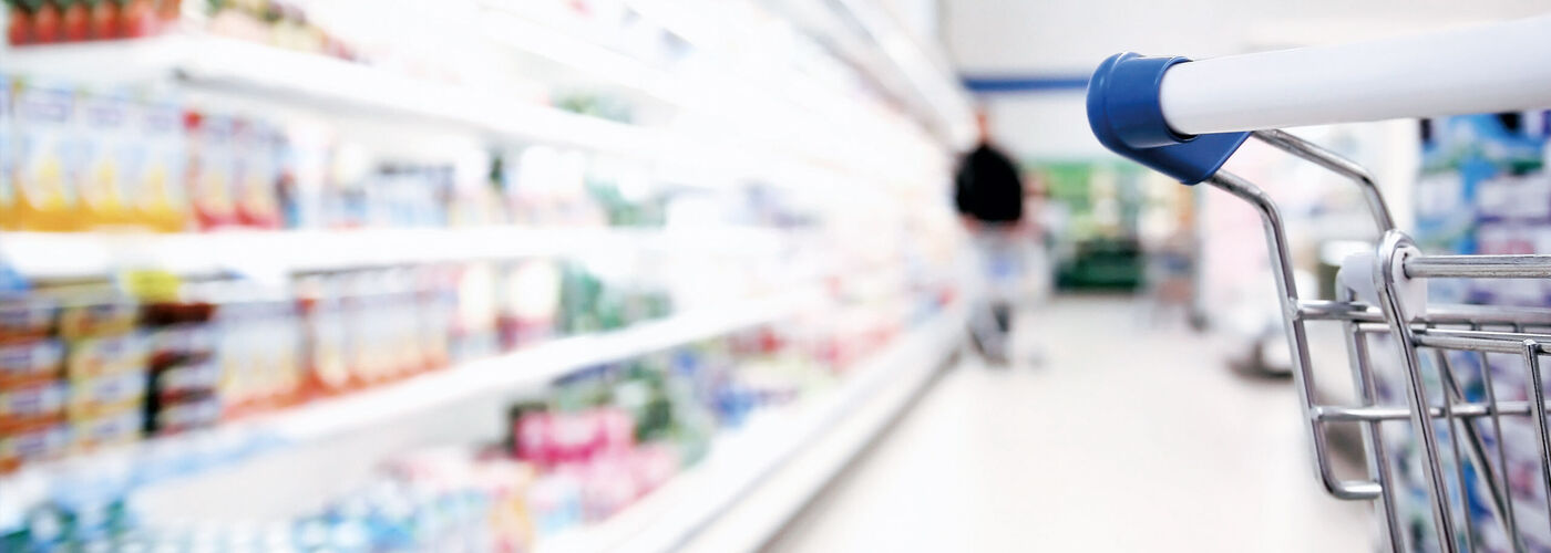 Półka w supermarkecie zamazana produktami, po prawej wózek sklepowy