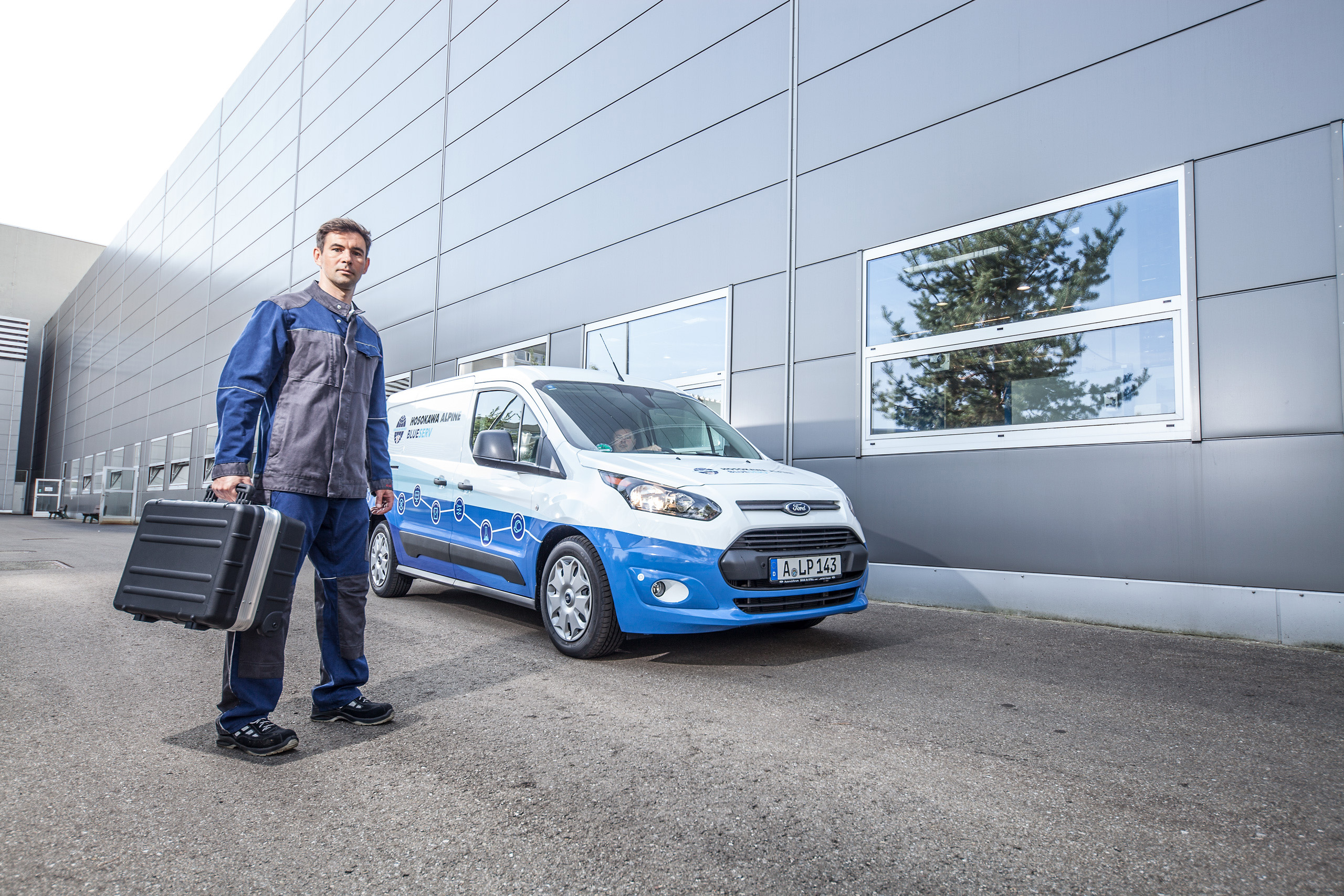 Pracownik Blueserv ze skrzynką narzędziową przed markowym samochodem Blueserv